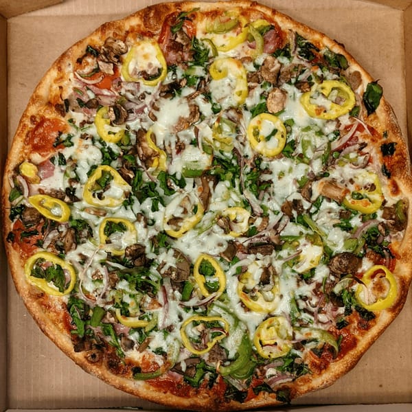 A whole pizza with melted cheese, mushrooms, green peppers, red onions, and spinach in a box.