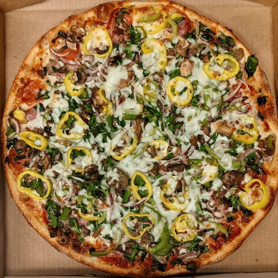 A whole pizza with melted cheese, mushrooms, green peppers, red onions, and spinach in a box.