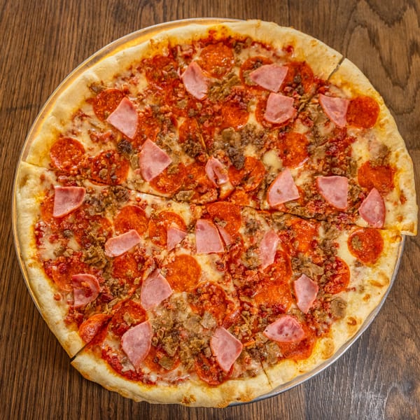 A whole meat lover's pizza with pepperoni, ham, and ground meat, sliced on a wooden table.