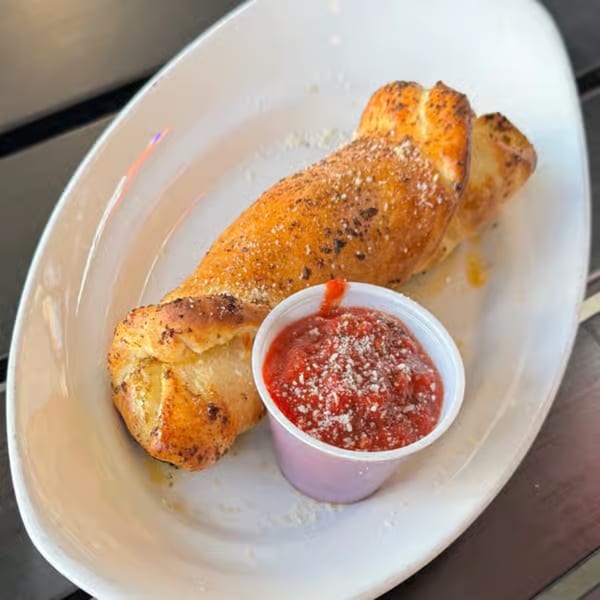 Golden-brown twisted breadstick, sprinkled with parmesan and herbs, served with a side of marinara sauce.