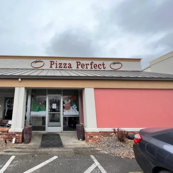 Exterior of Pizza Perfect restaurant with a red sign, glass doors, and a red wall.