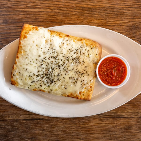 Cheesy bread with herbs and a side of marinara sauce on a white plate.