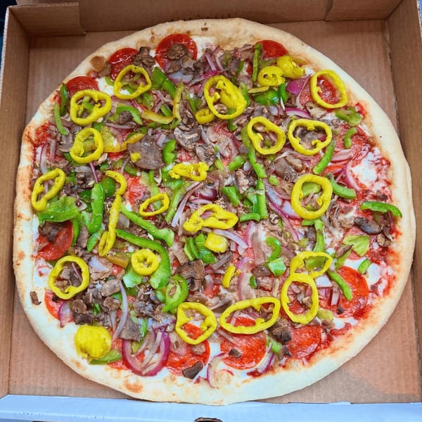 A whole pizza in a cardboard box, topped with pepperoni, mushrooms, onions, and colorful peppers.